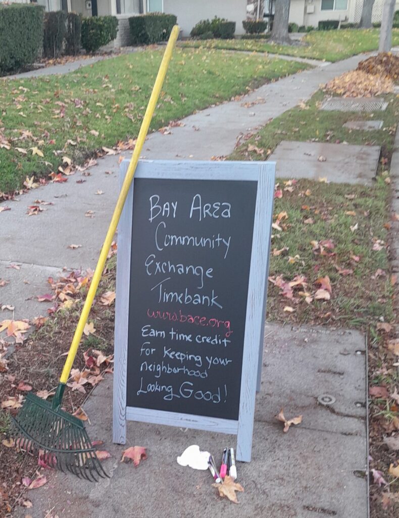 An image of a rake against an A-sign promoting timebanking during fall season in Bay Area neighborhood.